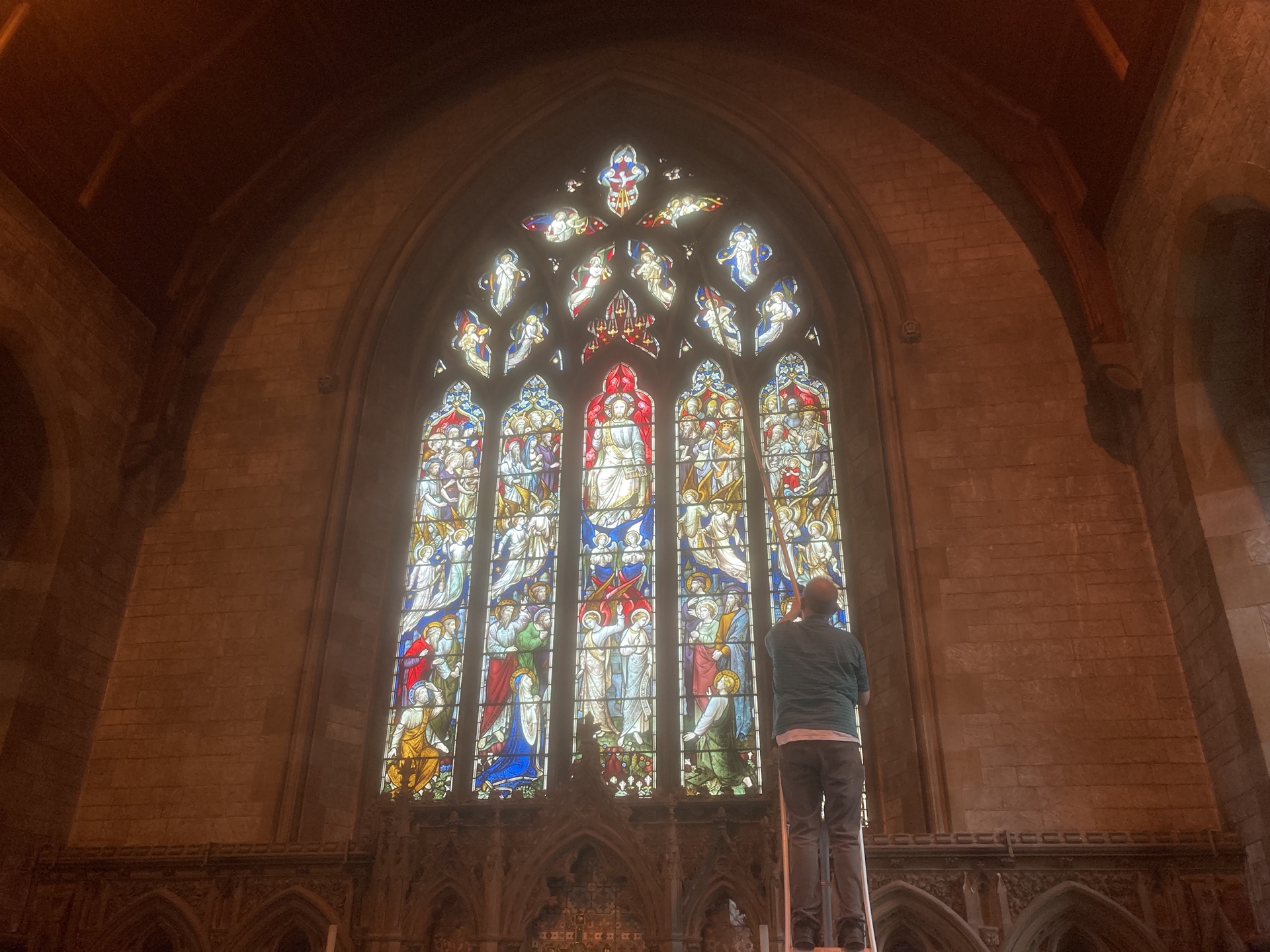 Man uses long pole to dust church window.